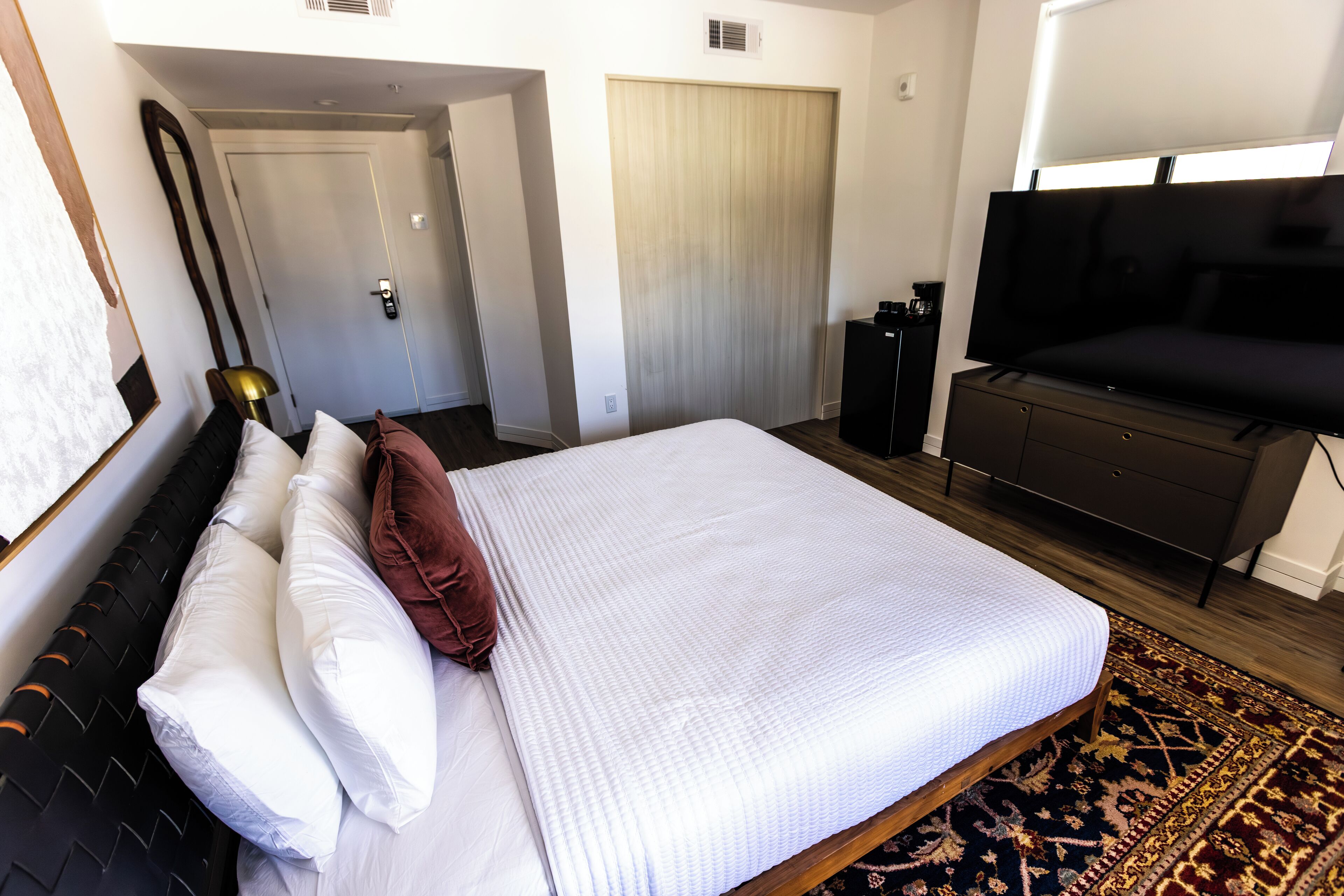 Ett hotellrum med en stor säng, en tv, en garderob och en dörr som leder till ett annat rum.