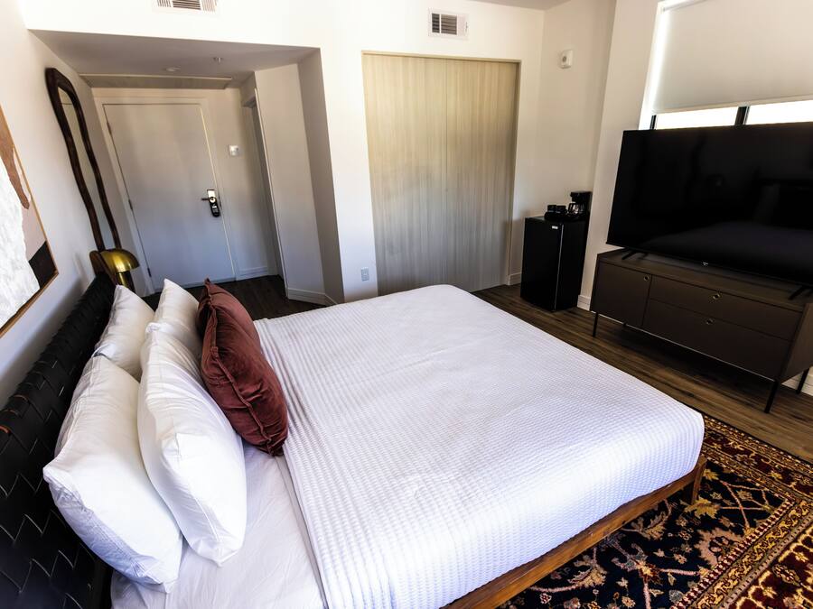 Ett hotellrum med en stor säng, en tv, en garderob och en dörr som leder till ett annat rum.