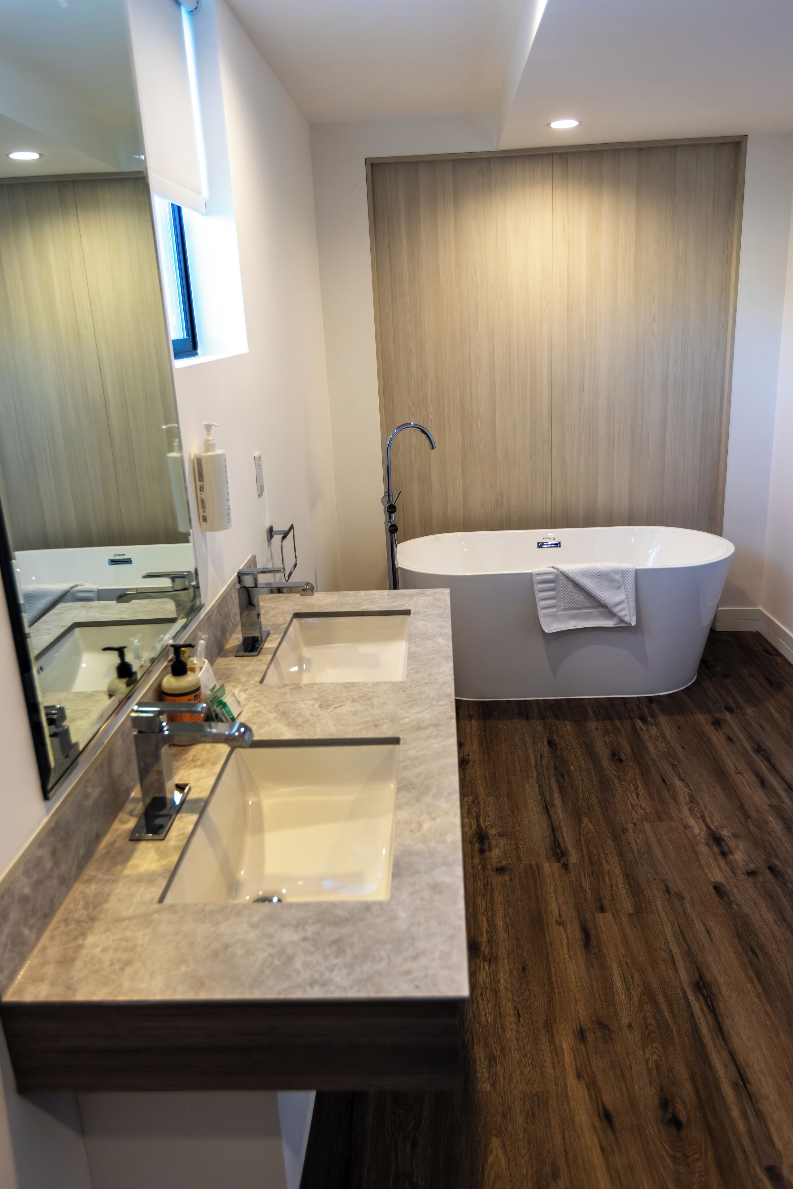 Un baño moderno con dos lavamanos, una bañera independiente y un espejo grande.