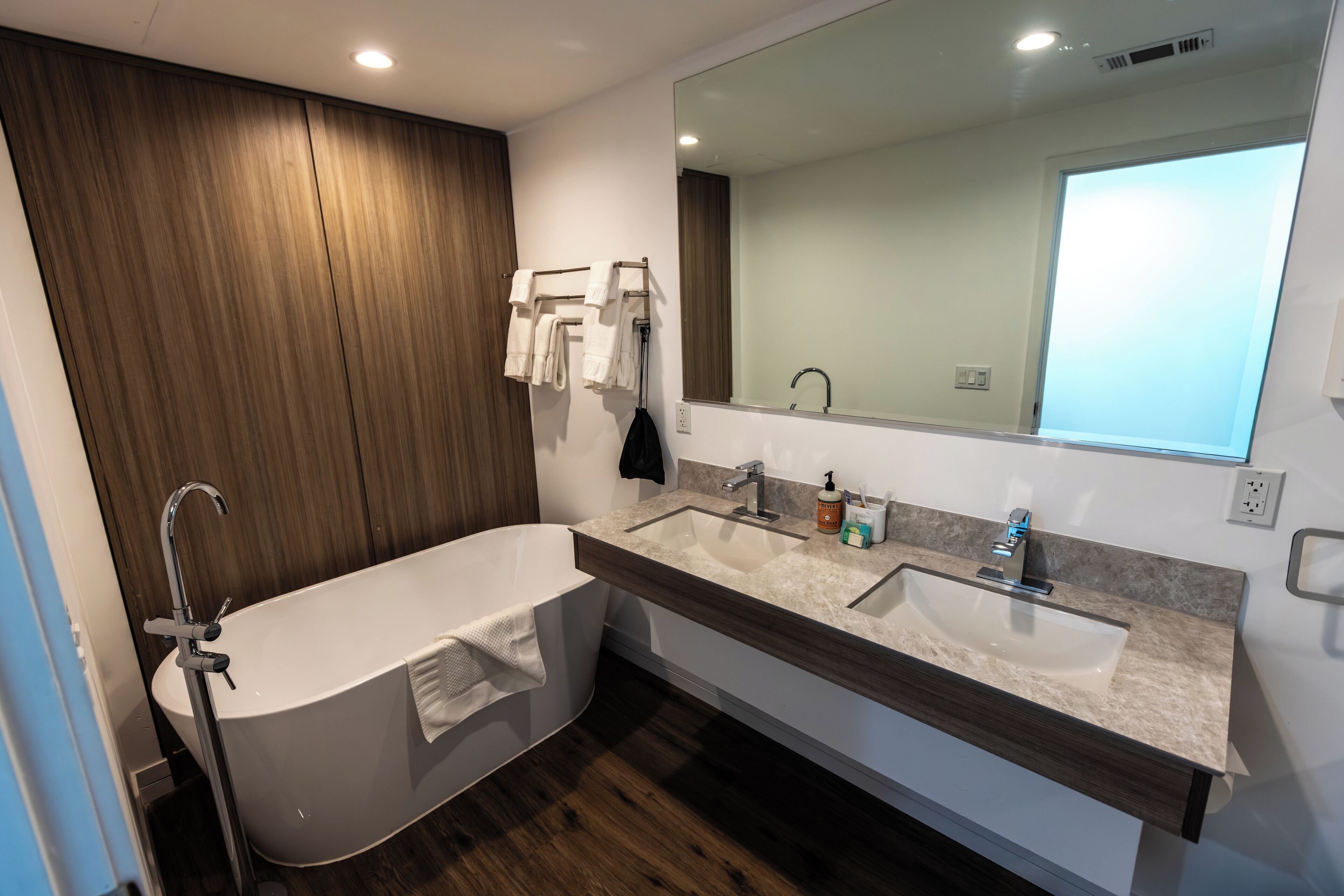 A modern bathroom with a freestanding bathtub, a double sink vanity, and a large mirror.