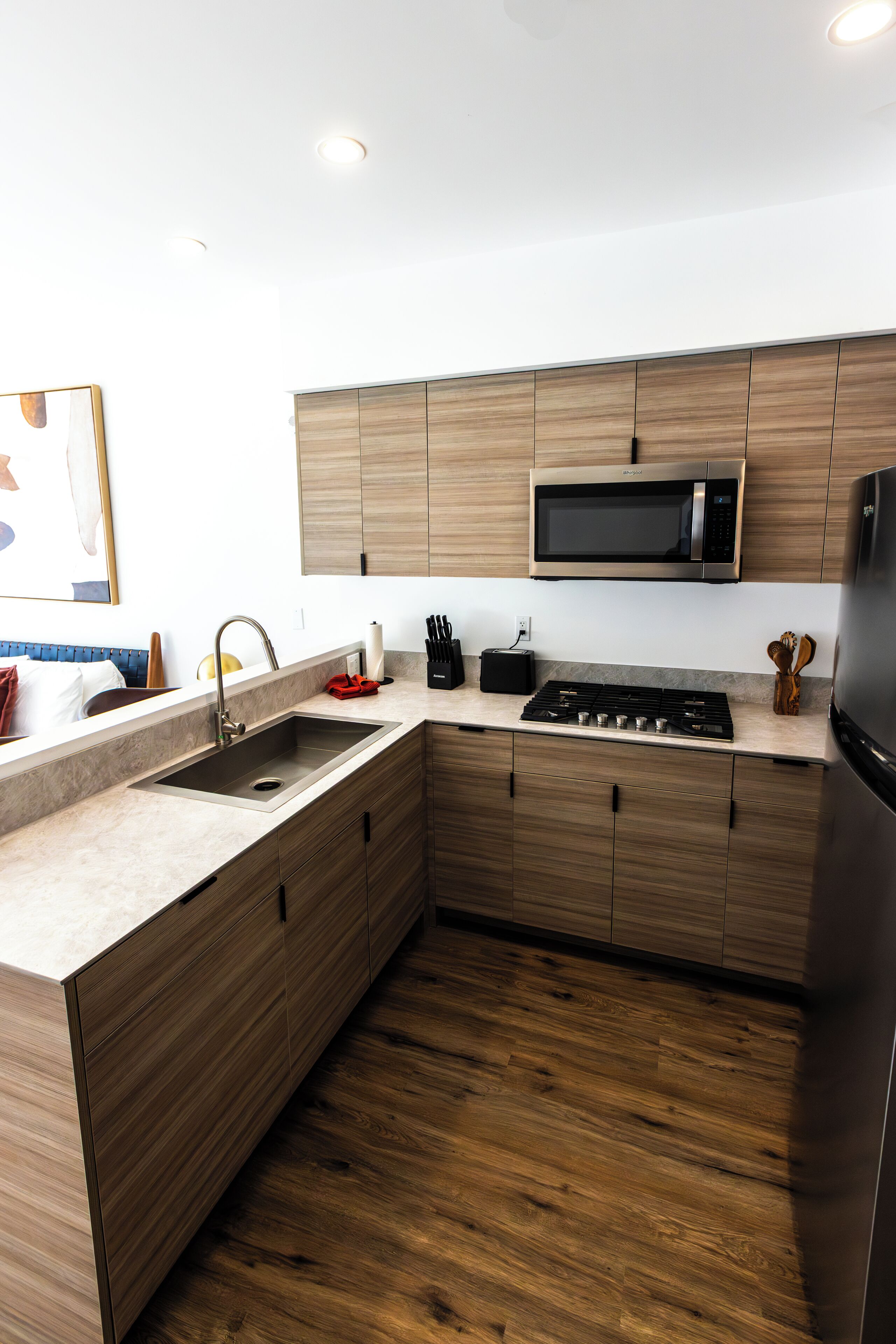 A modern kitchen with wooden cabinets, a stainless steel sink, a microwave, and a stove.