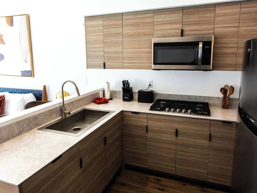 A modern kitchen with wooden cabinets, a stainless steel sink, a microwave, and a stove.