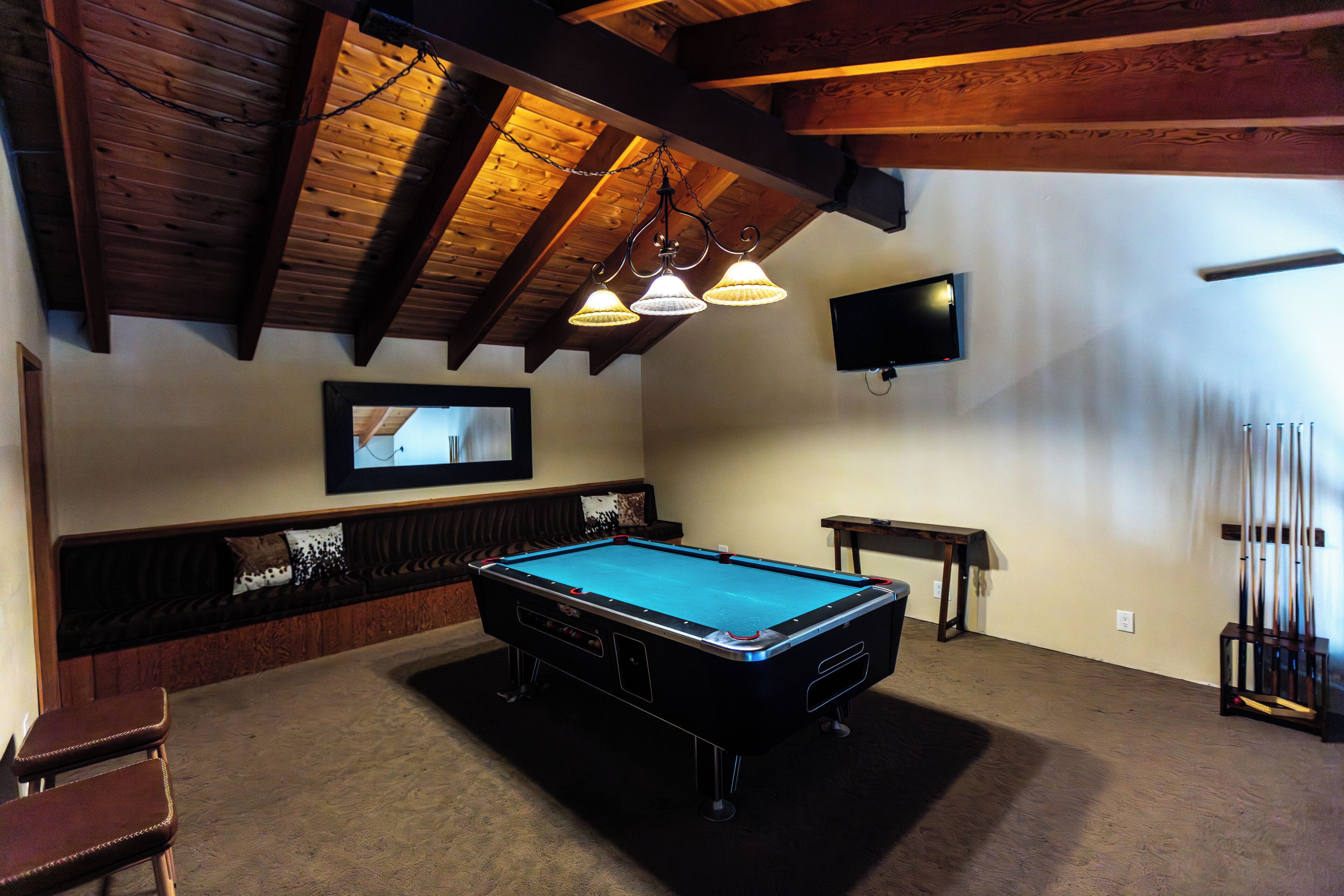 A pool table in a room with wooden beams, a television mounted on the wall, and a billiards rack.