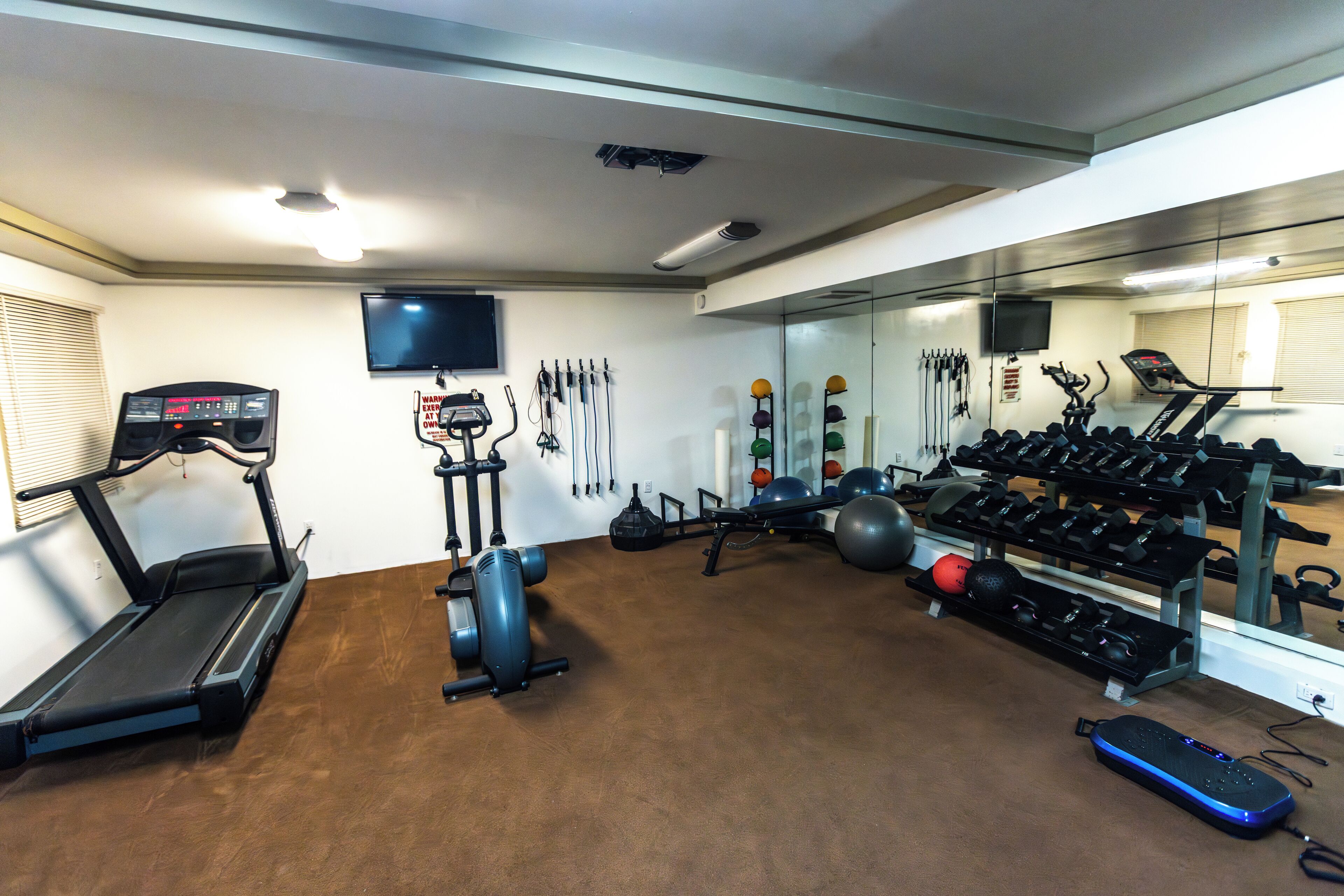 A gym with treadmills, an elliptical, a stationary bike, and various weights.