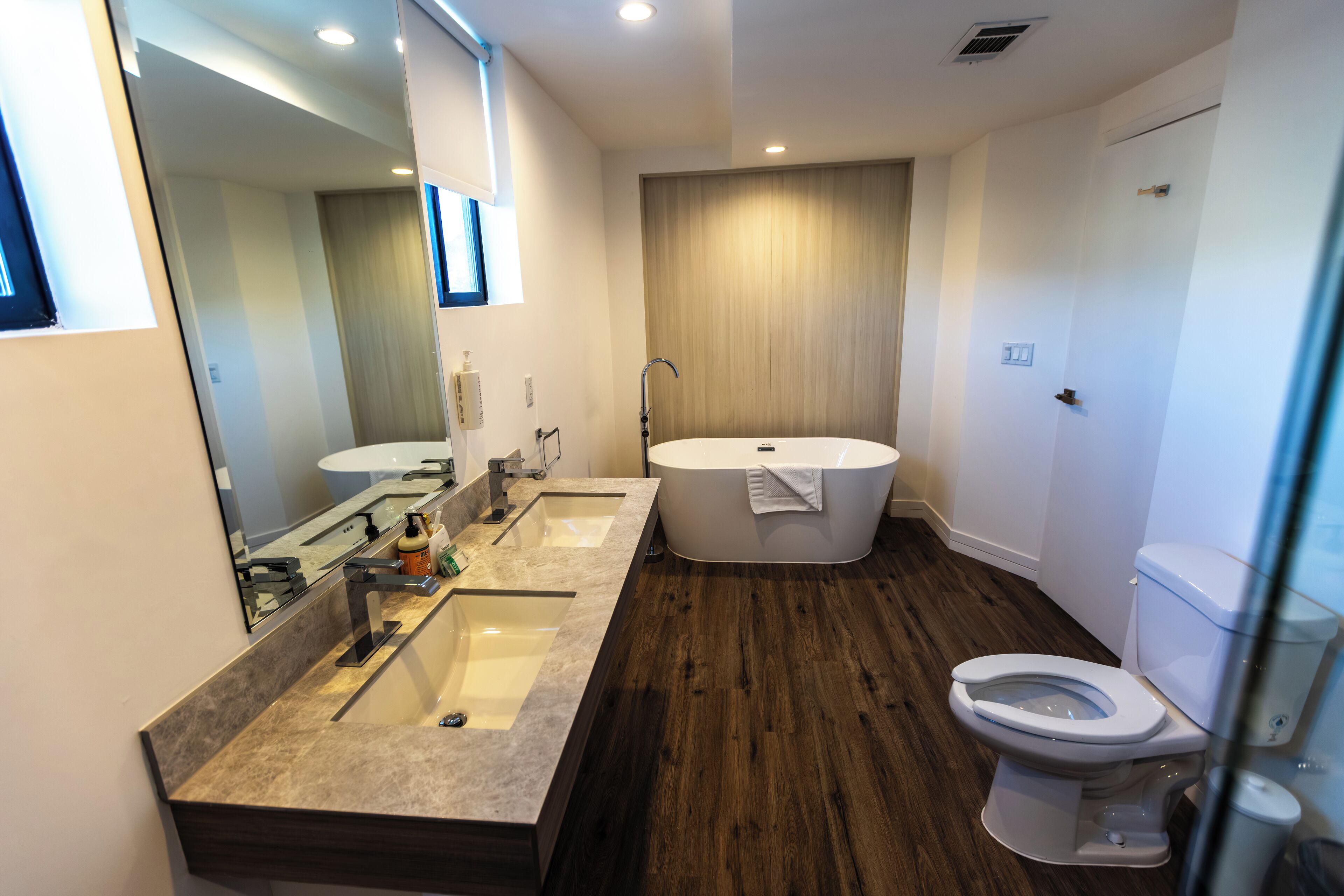 A modern bathroom with a double sink, a bathtub, and a toilet.