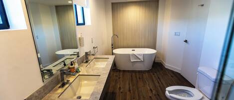 A modern bathroom with a double sink, a bathtub, and a toilet.