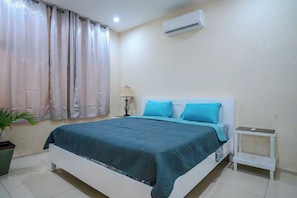 A bedroom with a bed, a bedside table, a lamp, and a potted plant. - The Island Nook Bim | Poolside Retreat Steps from Dover Beach & St. Lawrence Gap (St Lawrence Main Road)