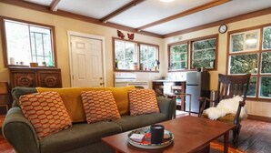 A cozy living room with a sofa, a coffee table, and a chair. There is a kitchen area with a refrigerator and a sink.