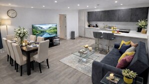 Ett modernt vardagsrum med en matplats, ett kök och en tv-skärm som visar ett vackert landskap.