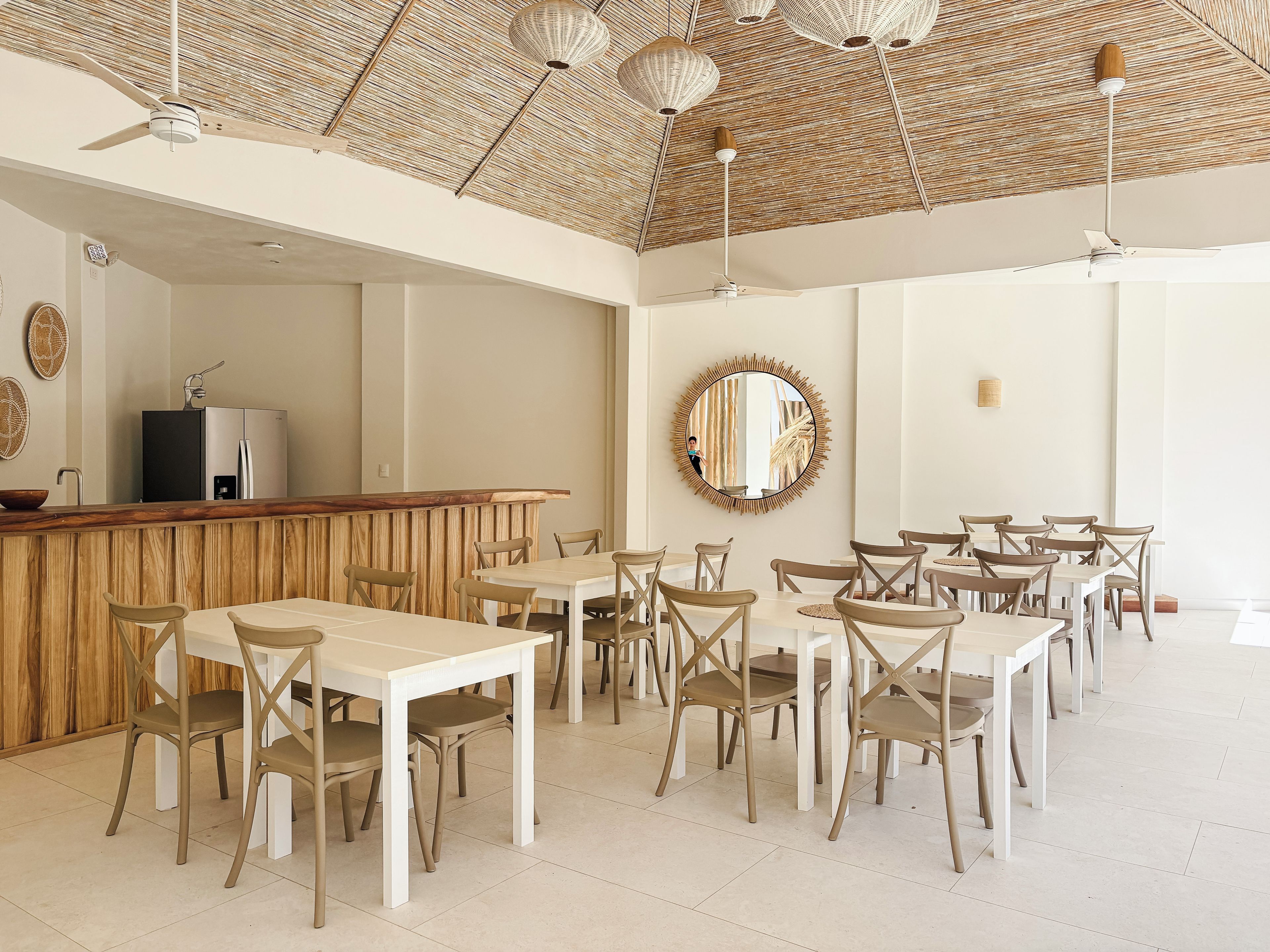 A spacious dining area with multiple tables and chairs, a wooden counter, and a ceiling with woven patterns.
