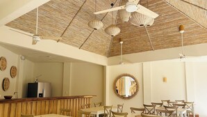 Ein geräumiger Essbereich mit mehreren Tischen und Stühlen, eine Holzdielendecke mit Gewebemuster und ein großer Spiegel an der Wand.