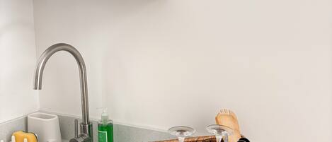 A kitchen with a stainless steel sink, a white countertop, a hanging plant, and a woven basket containing utensils.