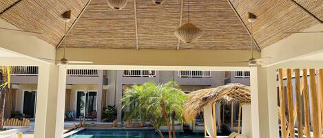 A poolside area with a thatched roof, seating, and a view of a swimming pool.