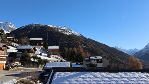 Een bergdorp met sneeuwbedekte daken en gebouwen, een helderblauwe lucht en een achtergrond van besneeuwde bergtoppen.
