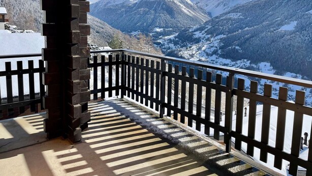 Een balkon met uitzicht op besneeuwde bergen en een heldere lucht.