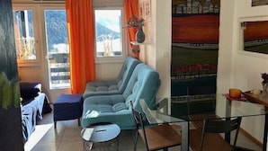 Ein Wohnzimmer mit einer Couch, Sesseln, einem kleinen Tisch und einem Fenster mit Vorhängen.