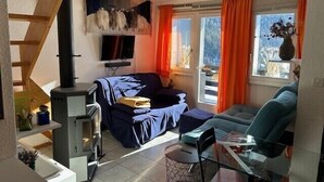 Ein Wohnzimmer mit Sofa, Glastisch, Fernseher und Kamin.