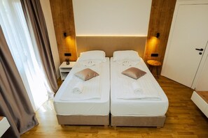 Una habitación con dos camas, suelo de madera, una mesita de noche y una puerta.