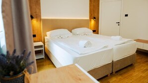 Hotellihuone, jossa on sänky, yöpöydät, puinen pääty, ovi ja pieni kasvi.