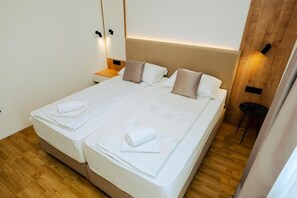 Un lit double avec du linge de lit blanc, une tête de lit en bois et une table de chevet avec une lampe.