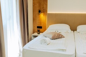 A hotel room with a bed, a nightstand, a wall-mounted light, and a window with curtains. - Vila Sunce Resort Konjic (Konjic)