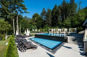 A swimming pool with lounge chairs and umbrellas, surrounded by trees and a building with a covered area. - Vila Sunce Resort Konjic (Konjic)