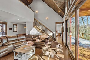 A spacious living room with a large sectional sofa, a wooden coffee table, and a modern chair. A wooden staircase leads to an upper level. - Winewood Haven at Eagles Nest - Fireplaces, King Ensuite, Firepit (Banner Elk)