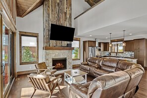 A spacious living room with a stone fireplace, leather sofa, and a large flat-screen TV mounted on a wooden beam. - Winewood Haven at Eagles Nest - Fireplaces, King Ensuite, Firepit (Banner Elk)