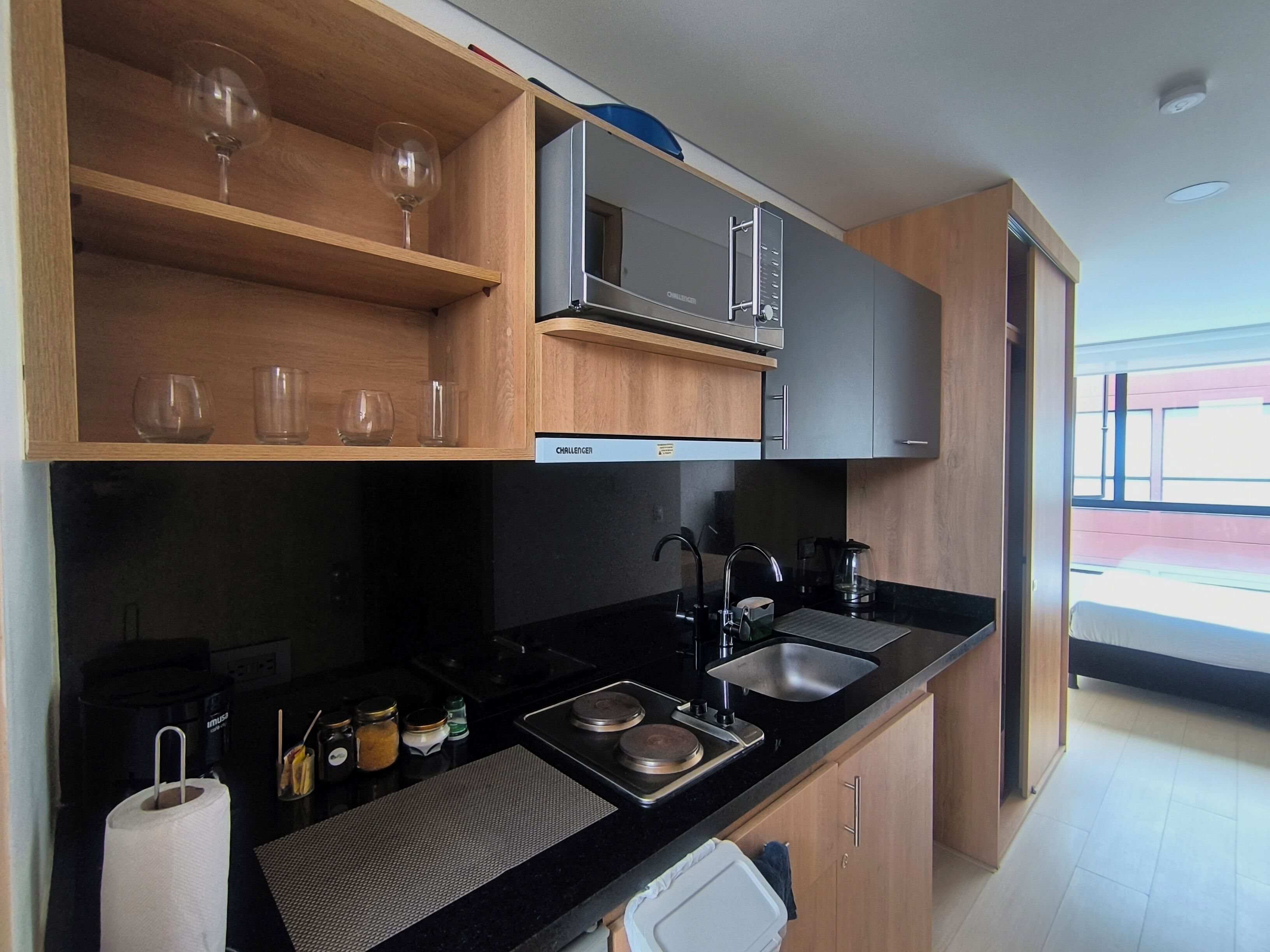 A modern kitchen with wooden shelves, a microwave, a sink, and a coffee maker.