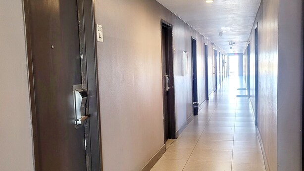 A long, narrow hallway with doors on both sides, tiled floor, and a ceiling with recessed lighting. - AVAION HOTEL LAX-SoFi Stadium (Inglewood)