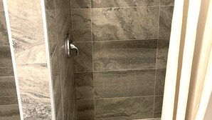 A shower with a curved showerhead and a handheld showerhead, tiled walls, and a shower curtain. - AVAION HOTEL LAX-SoFi Stadium (Inglewood)