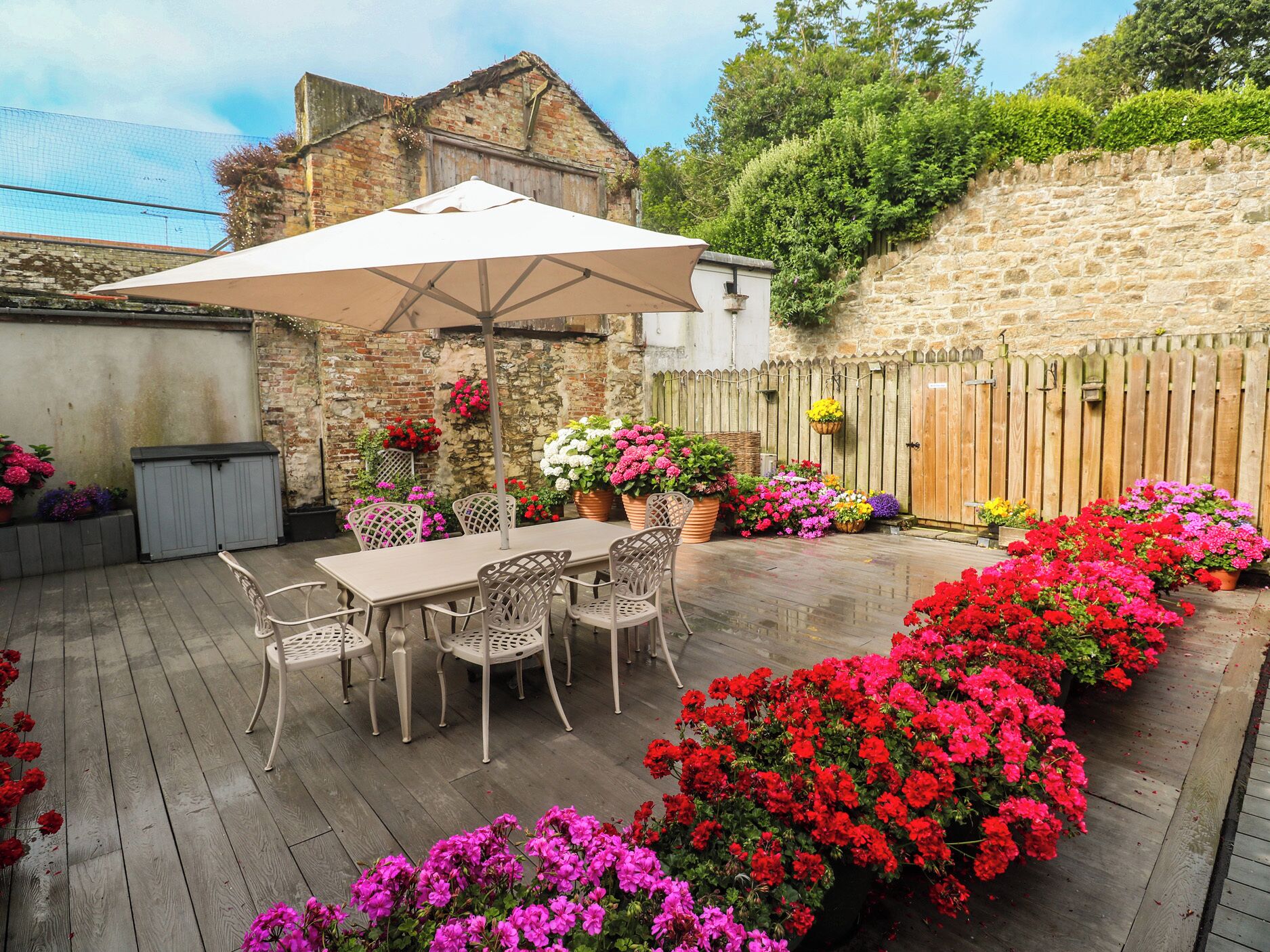 Un patio con mesa y sillas, rodeado de plantas y flores en macetas.