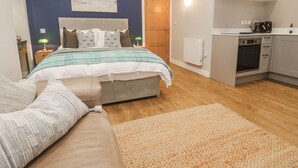 A bedroom with a bed, a bedside table, a nightstand, a lamp, a window, and a view of the outside. - Ammil Bespoke (St Ives)
