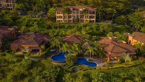 Een resort met meerdere gebouwen, een centraal gelegen zwembad en weelderige begroeiing.