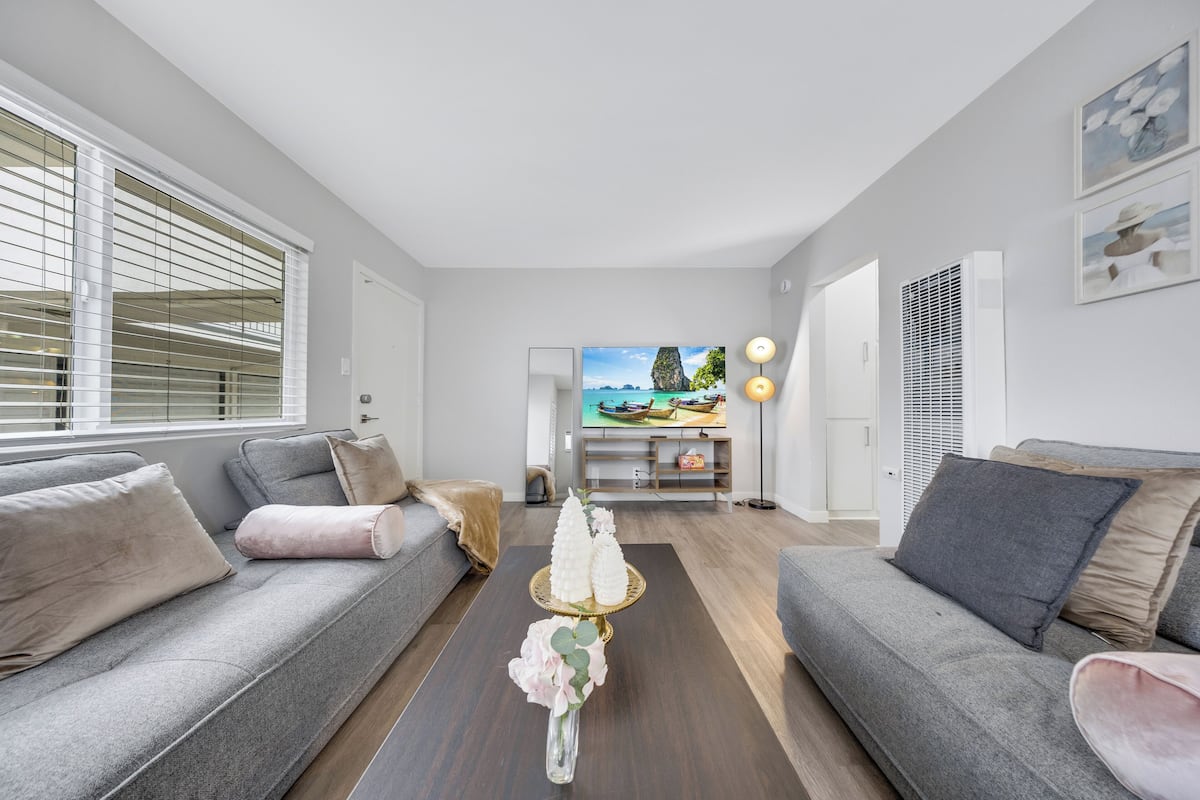 Un salon moderne avec des canapés gris, une table basse agrémentée d’objets décoratifs et un téléviseur en arrière-plan.