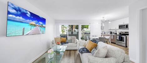 A modern living room with a glass coffee table, a beige sofa, and a large painting of a tropical beach scene.