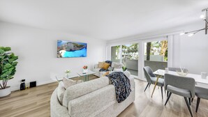 Een moderne woonkamer met een bank, een eettafel en stoelen. Er hangt een schilderij aan de muur en links staat een plant.