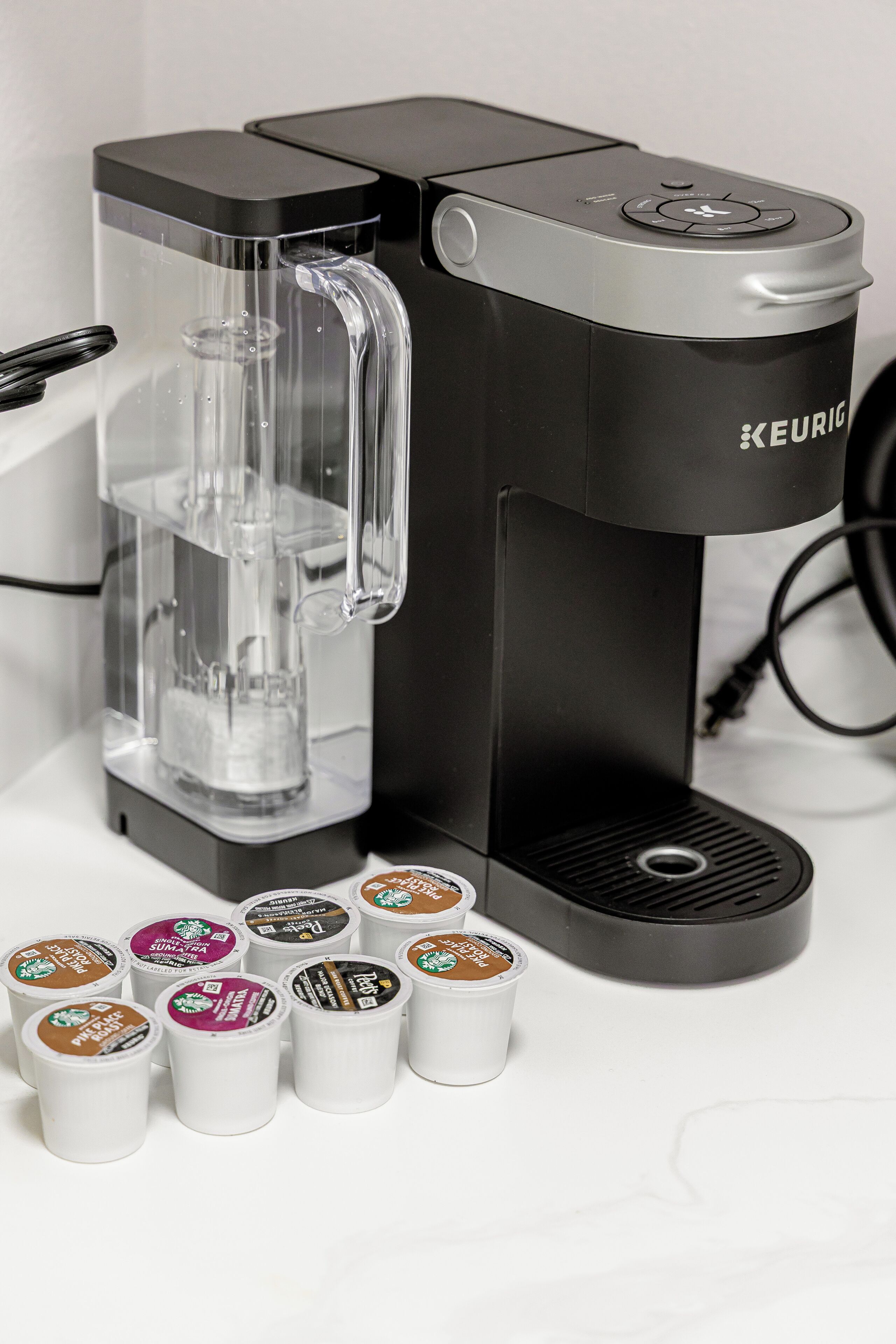 A Keurig coffee machine with a clear water reservoir and several coffee pods.