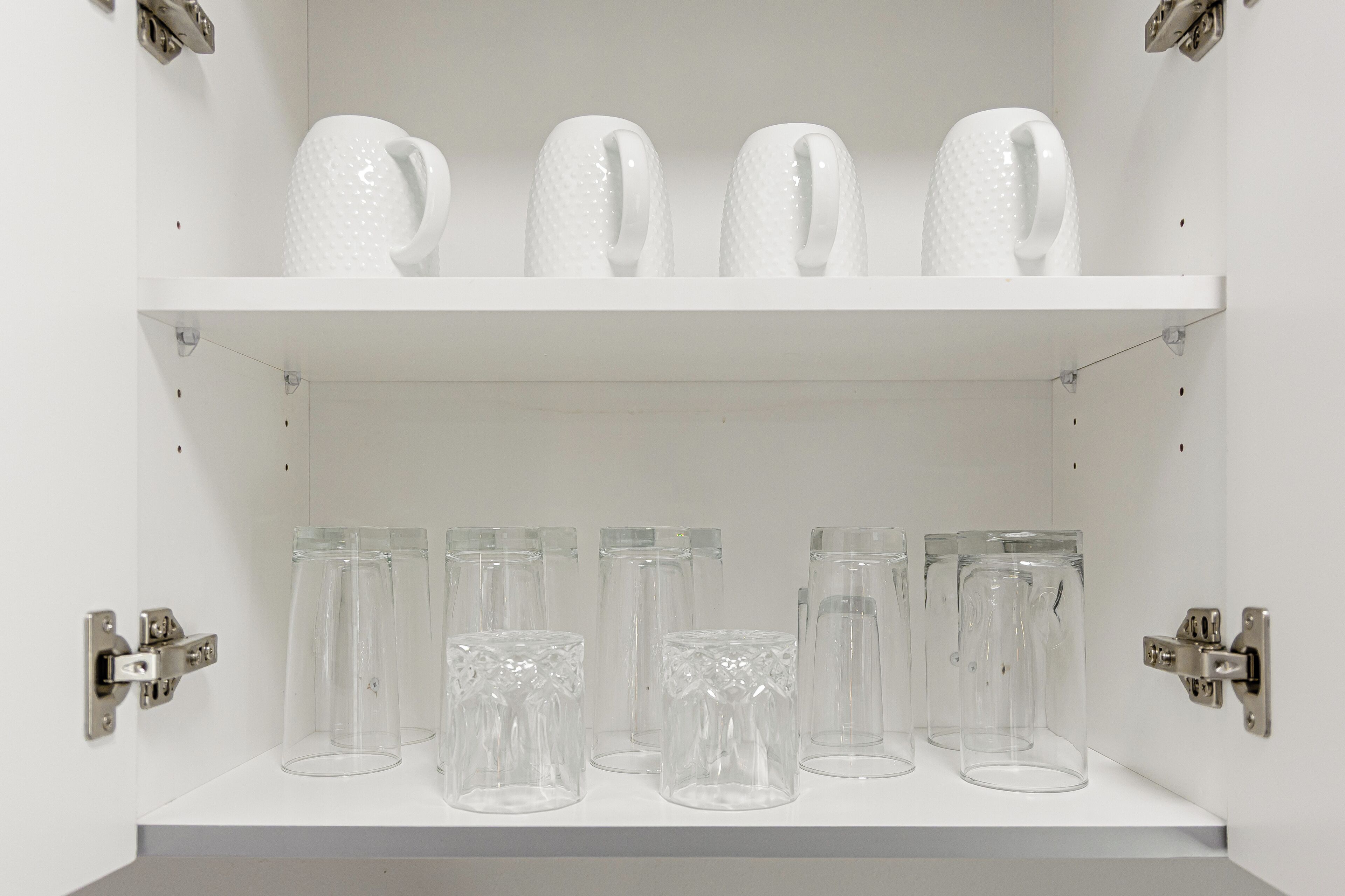 Une étagère blanche avec des verres en verre transparent et un pichet blanc.