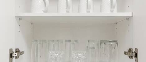 Une étagère blanche avec des verres en verre transparent et un pichet blanc.