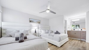 Een moderne slaapkamer met twee bedden, een plafondventilator, een nachtkastje met lamp en uitzicht op de badkamer.