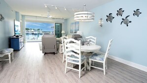Un coin repas avec une table et des chaises blanches, une vue sur le port de plaisance et un ventilateur de plafond.