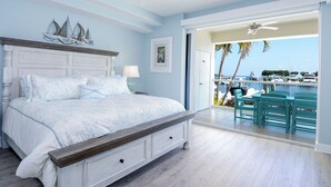 Ein Schlafzimmer mit Bett, Nachttisch, Fenster mit Blick auf den Hafen und Balkon mit Stühlen.