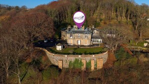 Ein großes, historisches Steinhaus mit gepflegter Rasenfläche und einer kreisrunden Steinmauer.