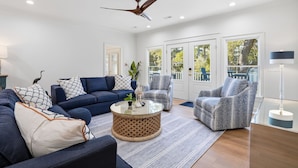 A modern living room with a blue sofa set, patterned armchairs, a round coffee table, and a ceiling fan. - Lowcountry Luxury and Charm on Edisto Beach (Edisto Island)