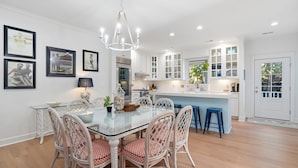 Une cuisine moderne avec des meubles blancs, une table à manger en verre, des chaises en osier et un coin bar bleu.