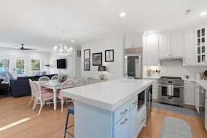 A modern kitchen with white cabinetry, a central island, and a dining area with white chairs and a table.