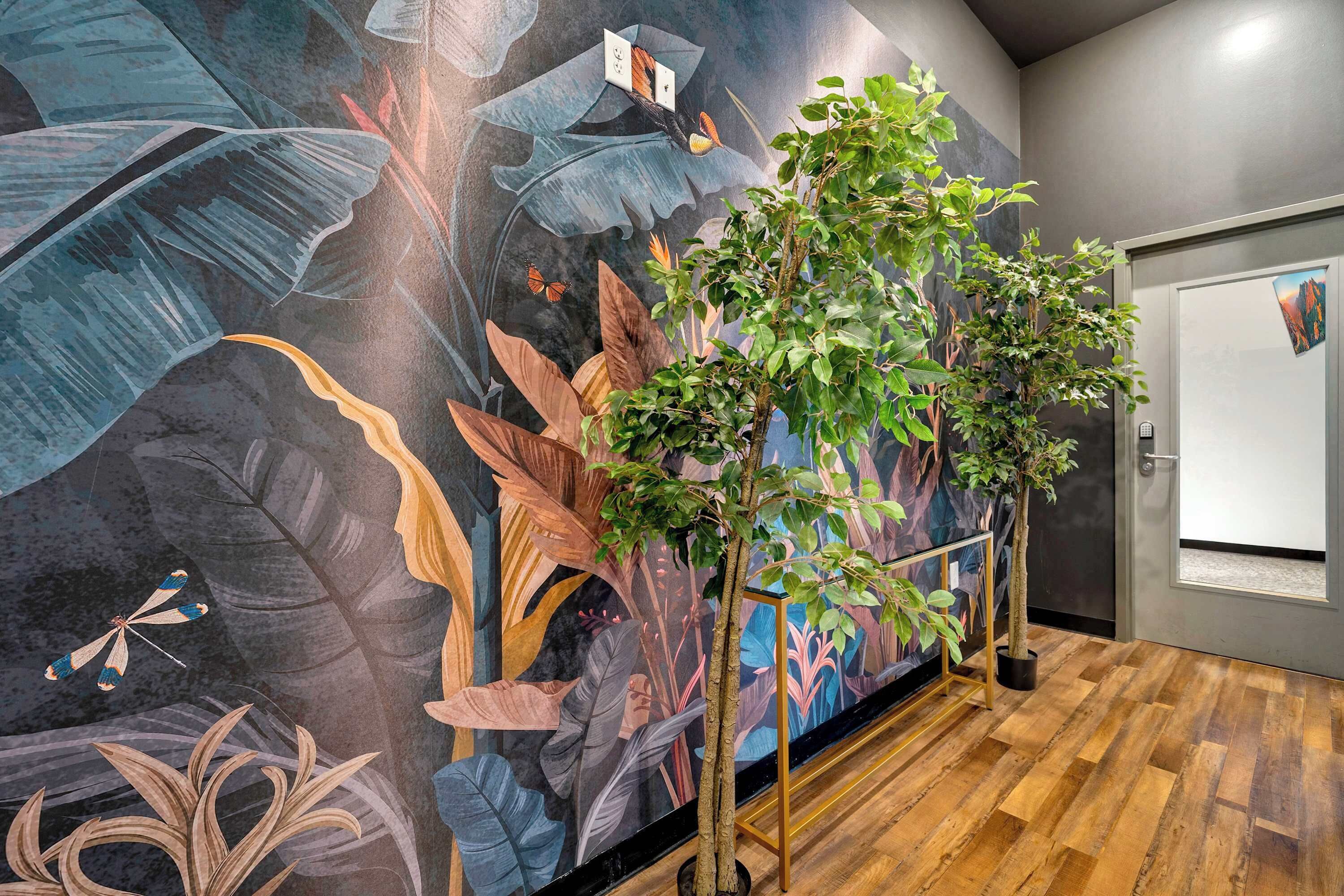 Quarto com um mural de folhagem tropical e borboletas, piso de madeira e plantas em vasos.