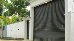 A building with a closed roller shutter garage door, a concrete wall, and a small window. - Crescent Bay Weligama (Weligama)