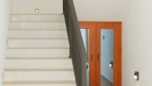 A staircase with a wooden handrail, a light fixture on the ceiling, and a door with a mirror. - Crescent Bay Weligama (Weligama)